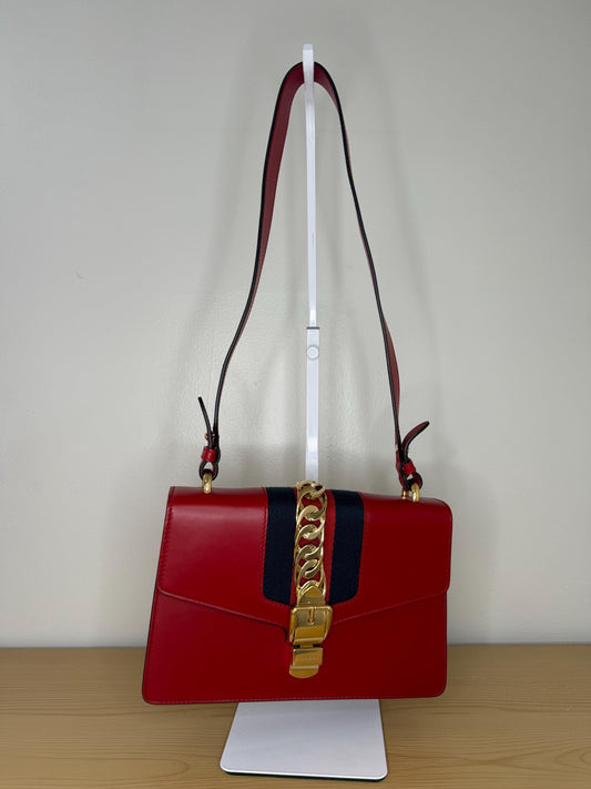 AUTHENTIC Gucci Red Leather Sylvie Sholuder Bag with gold-tone chain and buckle hardware.