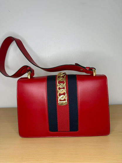 AUTHENTIC Gucci Red Leather Sylvie Sholuder Bag with gold-tone chain and buckle hardware.