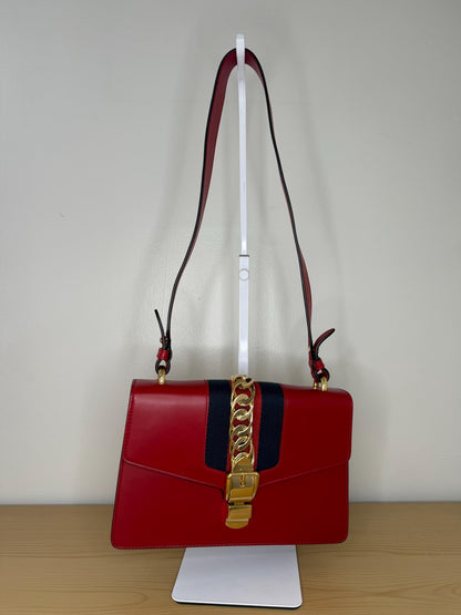 AUTHENTIC Gucci Red Leather Sylvie Sholuder Bag with gold-tone chain and buckle hardware.