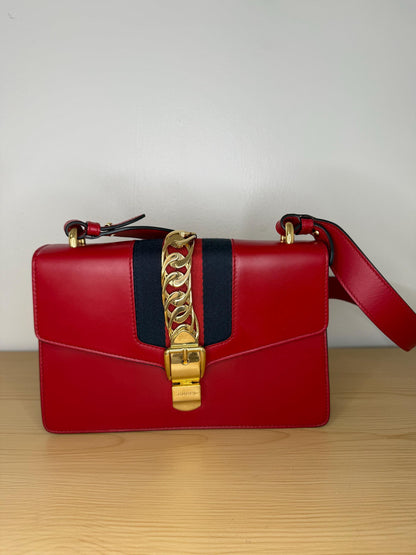 AUTHENTIC Gucci Red Leather Sylvie Sholuder Bag with gold-tone chain and buckle hardware.