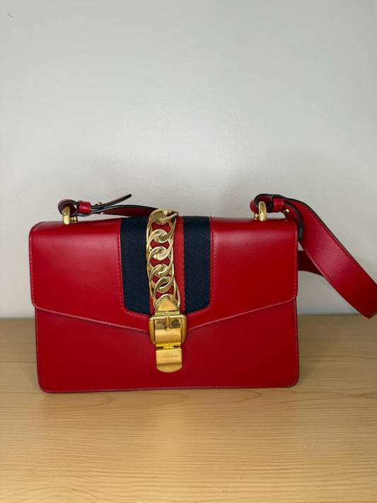 AUTHENTIC Gucci Red Leather Sylvie Sholuder Bag with gold-tone chain and buckle hardware.