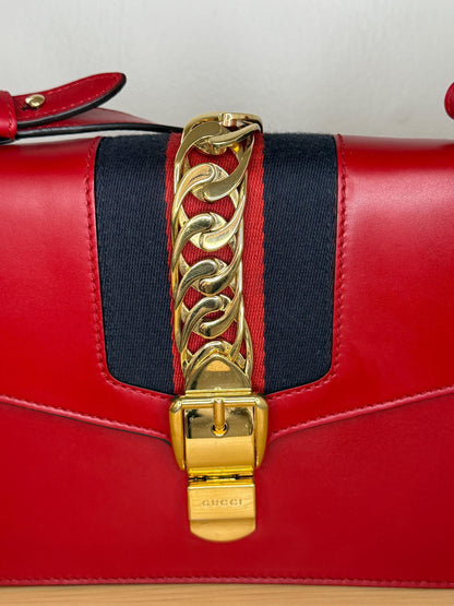 AUTHENTIC Gucci Red Leather Sylvie Sholuder Bag with gold-tone chain and buckle hardware.